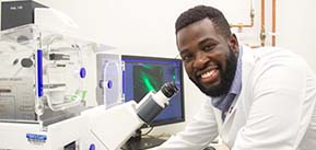 Image of Opeyemi Arogundade standing in front of a microscope