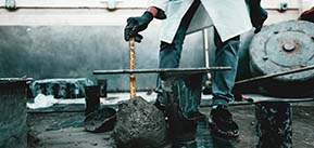person in a lab coat (only legs visible) sticking ruler into a chunk of wet concrete.