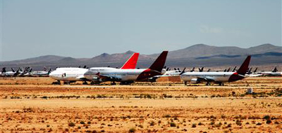 Three airplanes sit in the desert, with many more grounded planes in the distance behind them.