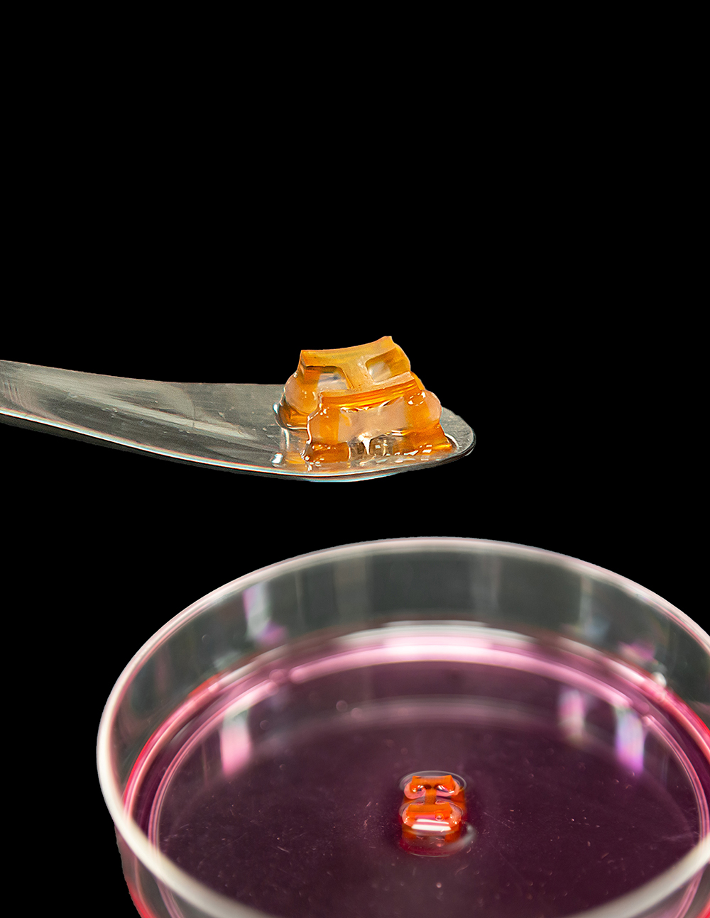 A tiny 3D orange block I held by a teaspoon over a petri dish.