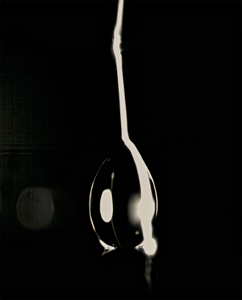 A drop of water appears black with a white line on one side against a black background.
