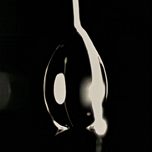 A drop of water appears black with a white line on one side against a black background.