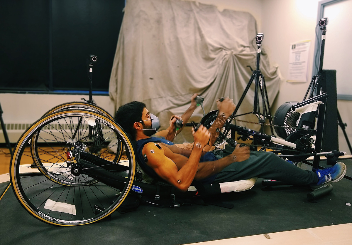 A person uses a stationary wheelchair handcycle in a research lab.