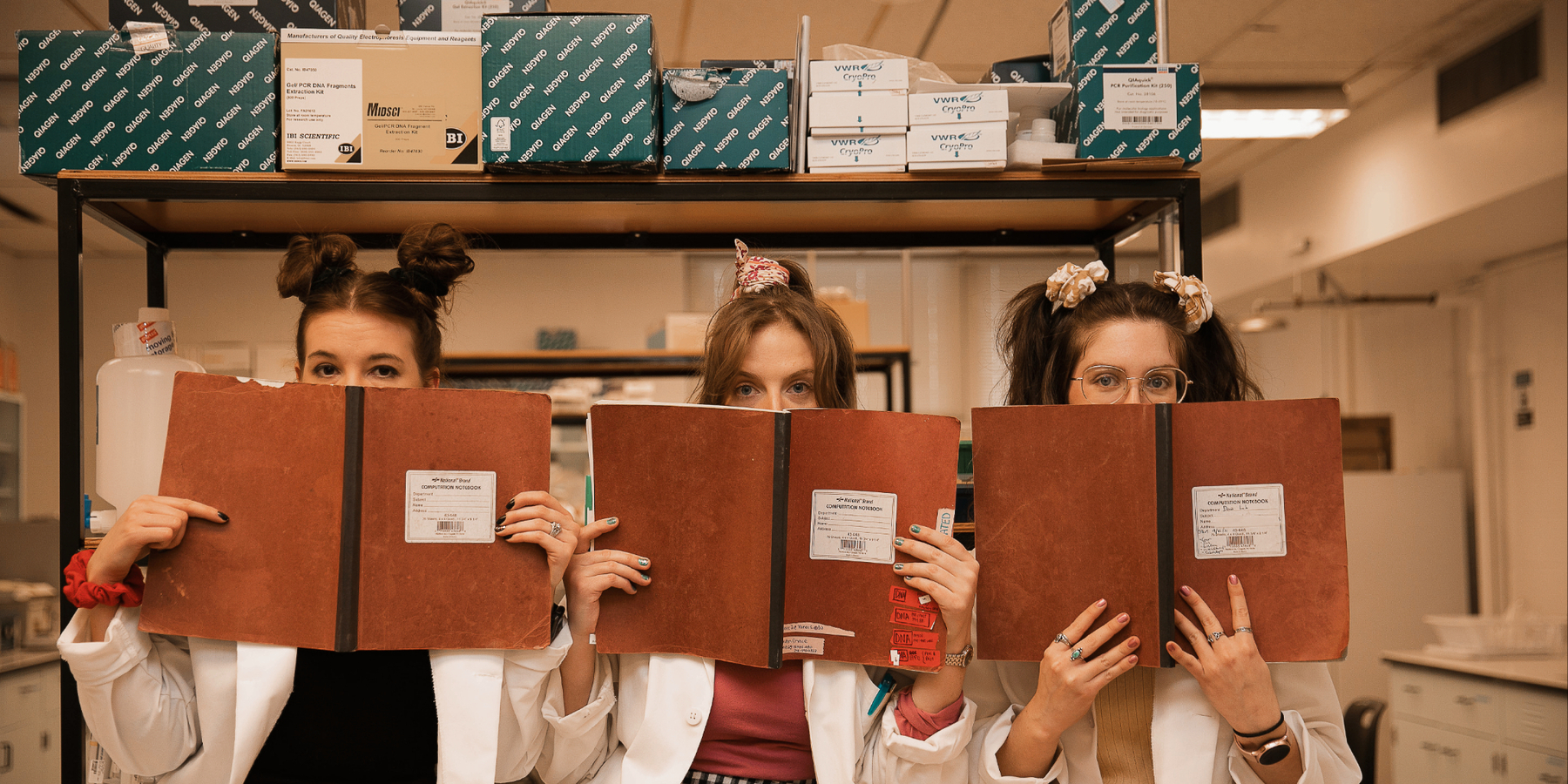 Three women hold report binders in front of their faces-- their eyes peer over at the viewer.
